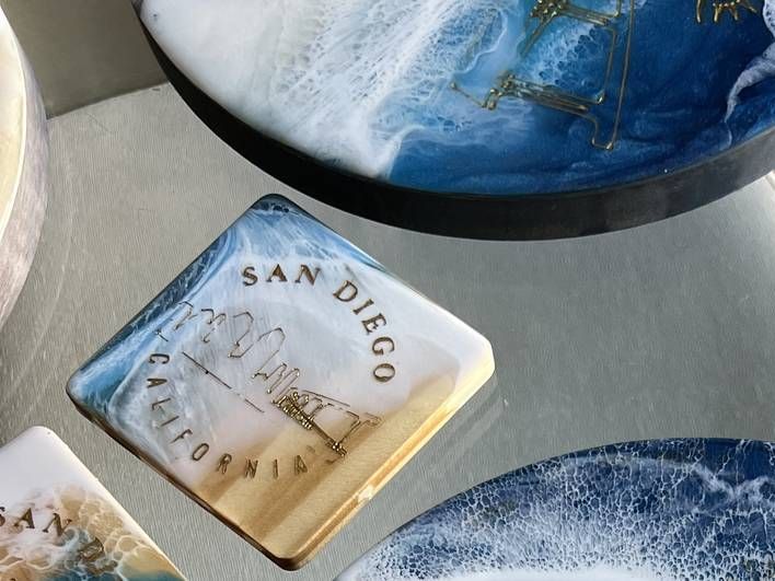A small square San Diego ocean resin piece with gold engraving beside a larger round