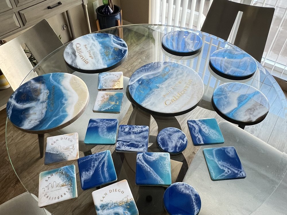A glass table covered with round and square ocean resin pieces in blue and white, several engraved San Diego California